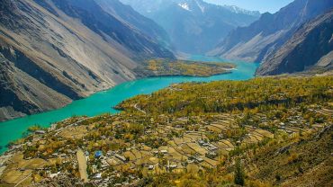 Panoramic view of Hunza Valley with terraced fields and Rakaposhi Peak under a clear blue sky.